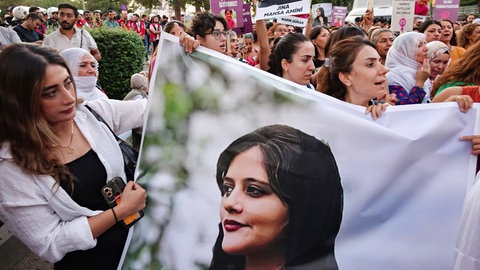 Demonstrierende tragen Plakate und ein großes Banner von Mahsa Amini während einer Gedenkveranstaltung in Diyarbakir.
