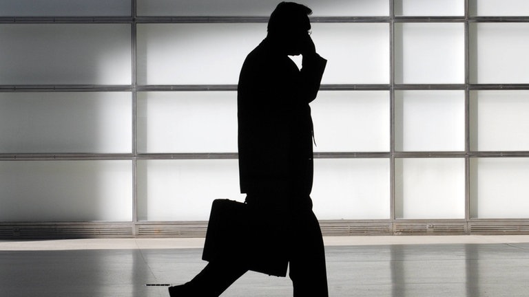 Silhouette eines Mannes mit Aktenkoffer telefoniert im Gehen