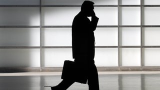 Silhouette eines Mannes mit Aktenkoffer telefoniert im Gehen