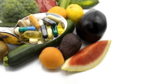 Ein Löffel voll mit Supplements vor Gemüse und Obst
