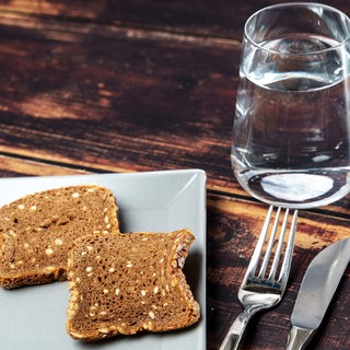 Glas Wasser neben einem Teller mit trockenem Brot