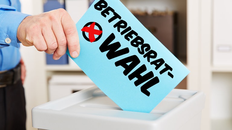 Hand mit Stimmzettel an Wahlurne für eine Betriebsratswahl
