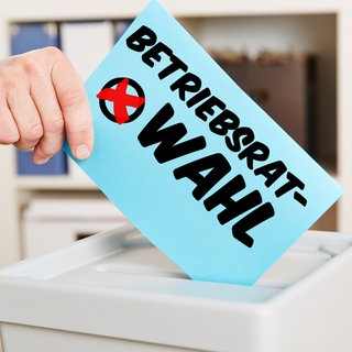 Hand mit Stimmzettel an Wahlurne für eine Betriebsratswahl