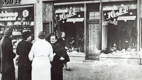 Passanten stehen im November 1938 in einer Stadt in Deutschland vor einem jüdischen Geschäft, dessen Schaufensterscheiben in der Reichsprogromnacht am 9. Nov. 1938 zerstört wurden.