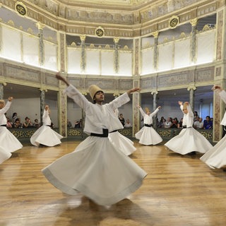 Tanzende Derwische. Eine Gruppe von Derwischen tanzt synchron in weißen Gewändern auf einem Holzfußboden umgeben von Zuschauern, Provinz Istanbul. Archivfoto.