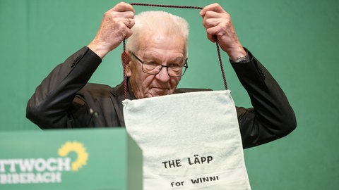 Winfried Kretschmann hängt sich beim politischen Aschermittwoch der Grünen 2023 einen großen Waschlappen um.