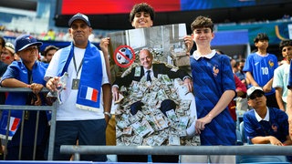 Französische Fußballfans halten bei der WM ein Bild von FIFA-Präsident Gianni Infantino mit Geldscheinen.