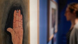Ein Frau steht in der Ausstellung „Menschen die noch hätten leben können“ in den Ausstellungsräumen der Sammlung Prinzhorn neben einem Werk des Künstlers Ludwig Berthold mit dem Arbeitstitel „Hand mit Auge“. 