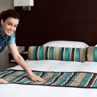Elegant housekeeping lady adding final touches to bedroom before customer arrival . Symbolfoto.