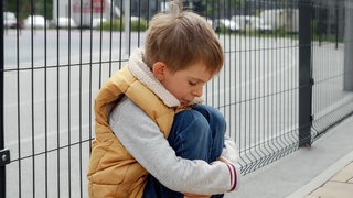 Porträt eines kleinen Jungen, der weint, während er alleine auf der Straße sitzt.