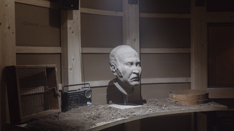 In einem dunklen Raum steht auf einem Tisch das Brustbild, neben ihm ein altes Radio.