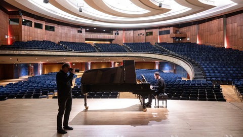 Igor Levit sitzt am Klavier vor leeren Rängen, der Fotograf Reiner Pfisterer steht vor ihm 