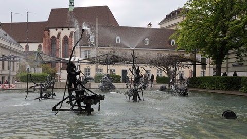 Das kinetische Kunstwerk wurde vom Schweizer Künstler Jean Tinguely geschaffen und ist eines von vielen Werken, die das Stadtbild von Basel prägen. Der Brunnen befindet sich auf dem Gelände des ehemaligen Stadttheaters, das 1975 abgerissen wurde. 