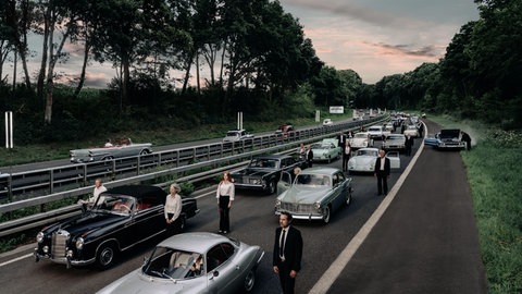 Oldtimer stehen im Stau auf Autobahn, Menschen stehen neben den Autos und schauen in die Ferne