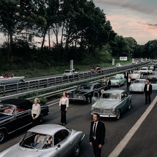 Oldtimer stehen im Stau auf Autobahn, Menschen stehen neben den Autos und schauen in die Ferne