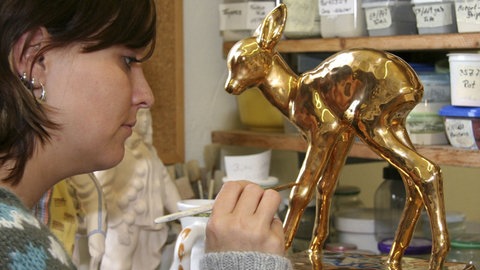 Keramikmalerin bemalt Bambi-Figur mit goldener Farbe.
