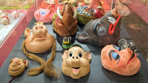 Schweinemasken und -figürchen in einer Vitrine des Stuttgarter Schweinemuseums. 
