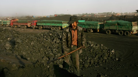 Chinesischer Arbeiter schaufelt Kohle in einer Industrielandschaft in Baotou, Innere Mongolei, umgeben von sandigen Schluchten.