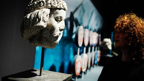 Eine Frau steht in den Reiss-Engelhorn-Museen in der Sonderausstellung „Die Normannen" (2022) neben einer Steinskulptur von Wilhelm dem Eroberer aus dem 14 Jahrhundert.