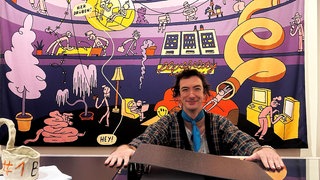 Comickünstler*in Dominik Wendland sitzt an einem überdimensionierten Schreibtisch mit riesigem Aktenordner und gewaltiger Kaffeetasse