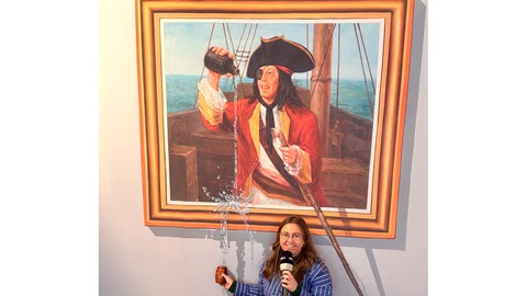 Eine Frau mit Mikrofon steht vor einem bunten Bild