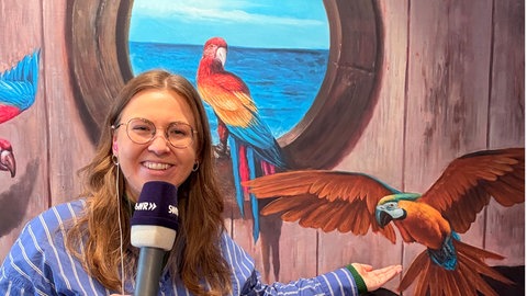 Eine Frau mit Mikrofon steht vor einem bunten Bild