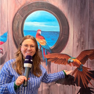 Eine Frau mit Mikrofon steht vor einem bunten Bild