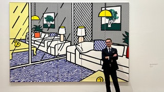 Ein Mann steht vor einem großen Pop-Up-Bild von Roy Lichtenstein