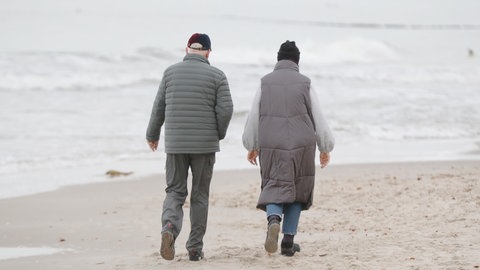 Alte Menschen laufen am Strand entlang