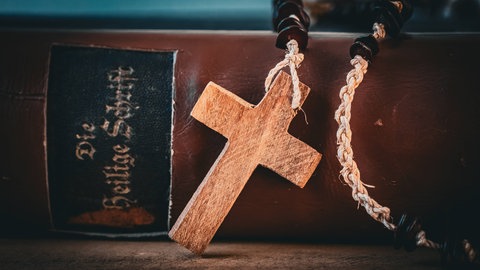 Eine Kreuzkette lehnt an einer alten Bibel.