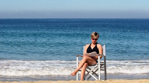 Eine Frau liest ein Buch am Meer