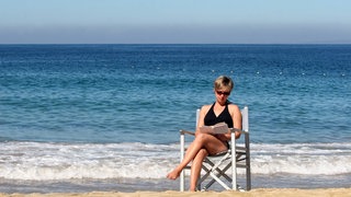 Eine Frau liest ein Buch am Meer