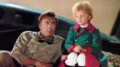 Der Pilot und der kleine Junge kommen ins Gespräch. Die Aufnahme stammt aus dem 1974 veröffentlichten britisch-amerikanischer Musikfilm. Steven Warner spielte die Titelrolle, Richard Kiley den Piloten.