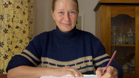 Illustratorin Kat Meschnik sitzt an einem Tisch, dabei zeichnet sie mit Tusche. 