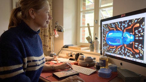 Illustratorin Kat Menschik sitzt vor einem Computer, um eine Zeichnung von ihr mit Farbe zu versehen