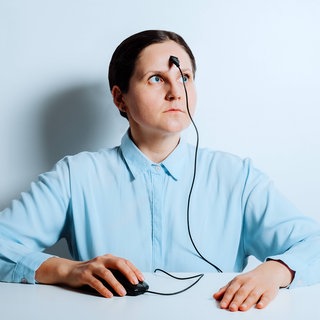 Frau mit PC-Maus und Kabel auf der Strin am Bürotisch