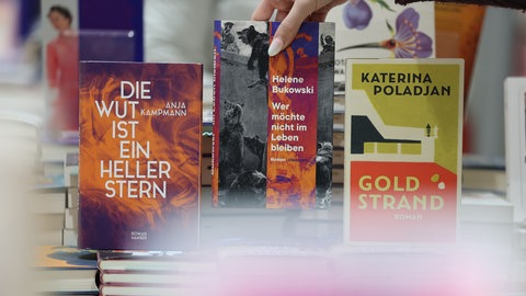 Eine Frau nimmt eines der Bücher "Die Wut ist ein heller Stern" ( Anja Kampmann), "Wer möchte nicht im Leben bleiben" (Helene Bukowski) und "Goldstrand" (Katerina Poladjan) in einem Buchladen in die Hand. 
