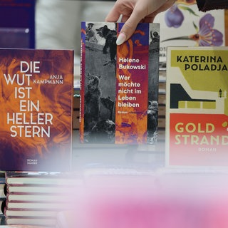 Eine Frau nimmt eines der Bücher "Die Wut ist ein heller Stern" ( Anja Kampmann), "Wer möchte nicht im Leben bleiben" (Helene Bukowski) und "Goldstrand" (Katerina Poladjan) in einem Buchladen in die Hand. 