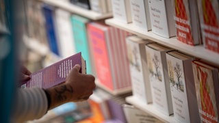 Person steht vor einem Bücherregal, hält ein Buch, um den Klappentext zu lesen