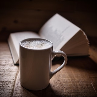 Symbolbild: Eine Tasse Kaffee mit einem aufgeschlagenen Buch.