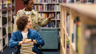 Mädchen hilft ihrem Kollegen im Rollstuhl bei der Auswahl eines Buchprojekts