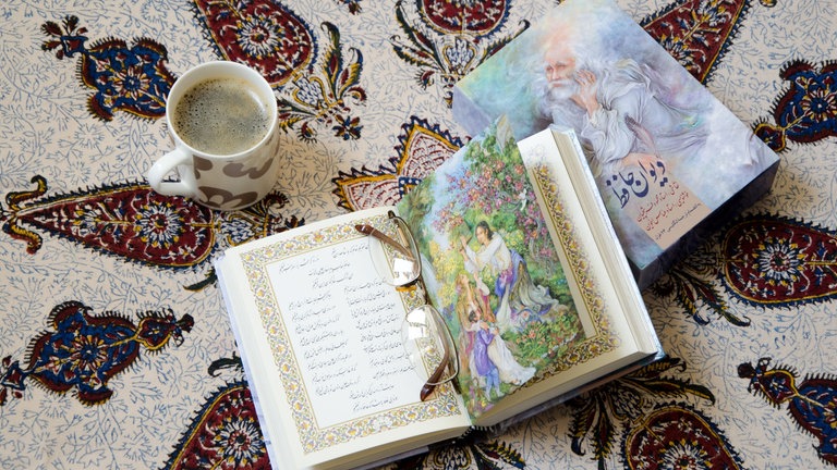 Divan-e-Hafez Buch, Gedichte des Iranischen Poeten Hafez geöffnet auf traditionellem Tischtuch mit Kaffeetasse