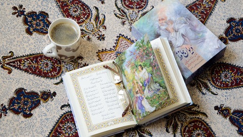 Divan-e-Hafez Buch, Gedichte des Iranischen Poeten Hafez geöffnet auf traditionellem Tischtuch mit Kaffeetasse