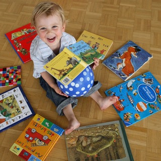 Kleinkind inmitten von Büchern auf dem Boden sitzend