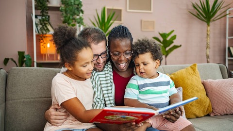 Eine Familie liest gemeinsam ein Buch im Wohnzimmer.