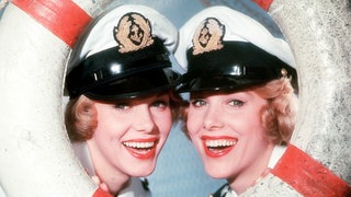 Die jungen Kessler-Zwillinge blicken lächelnd durch einen Rettungsring.