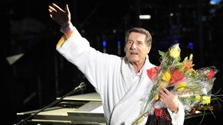 Der Sänger Udo Jürgens mit Bademantel und Blumen auf der Bühne