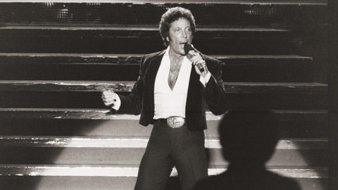 Schwarz-weiß Bild von Tom Jones, wie er auf der Bühne steht und singt.