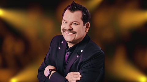 Comedien Ingo Appelt vor einem dunklen Hintergrund mit gelb-orangenen Spots