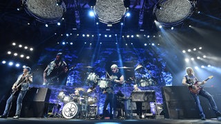 Die Musiker der Band "Deep Purple" stehen in einem blauen Licht auf der Bühne und machen Musik.